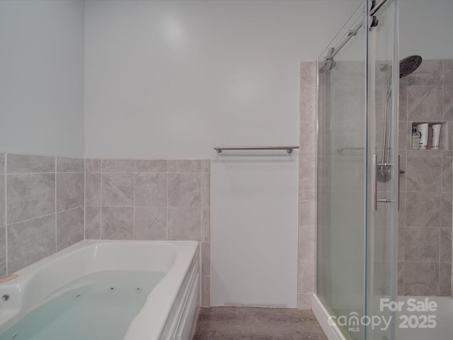 bathroom with a tub with jets, wood finished floors, and a shower stall