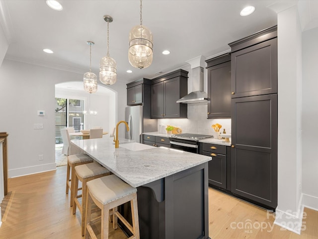 1409 Kenilworth Ave, Charlotte, NC 28203 - kitchen featuring wall chimney exhaust hood, stainless steel appliances, arched walkways, a breakfast bar area, and a center island with sink