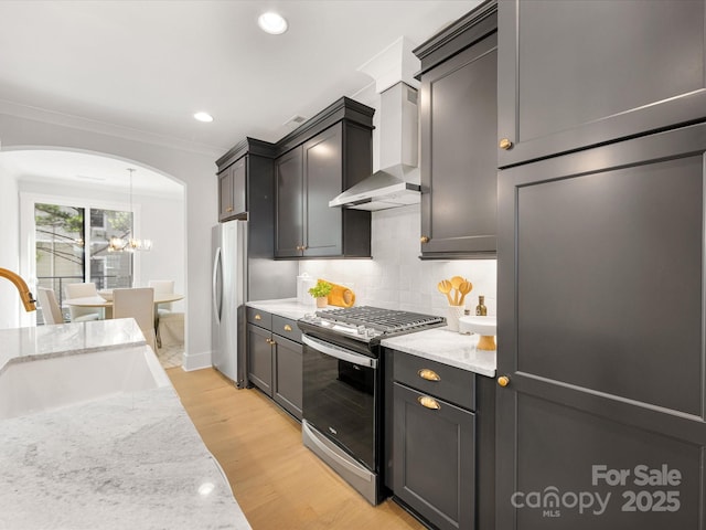 1409 Kenilworth Ave, Charlotte, NC 28203 - kitchen with appliances with stainless steel finishes, wall chimney range hood, arched walkways, light stone counters, and light wood-type flooring