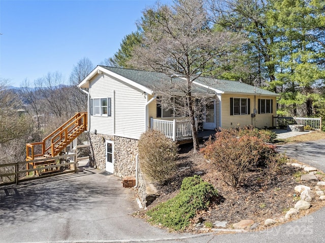 view of front of house with stairs, aphalt driveway, a porch, and stone siding