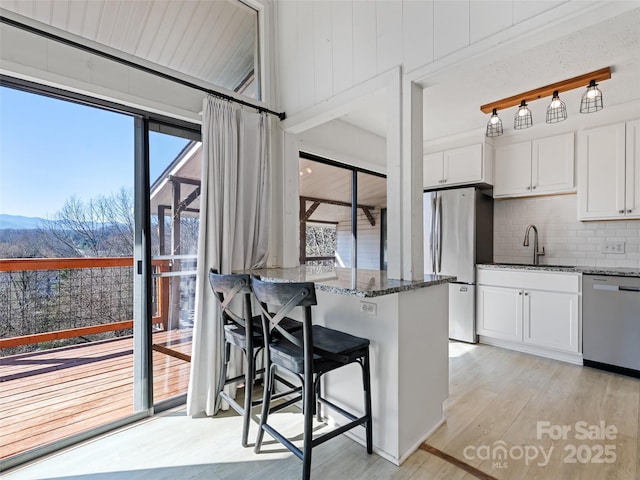 kitchen with dark stone countertops, light wood-style floors, white cabinets, stainless steel appliances, and a sink