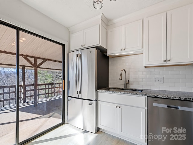 kitchen with a sink, backsplash, white cabinetry, stainless steel appliances, and dark stone counters