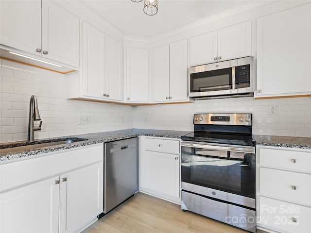 kitchen featuring a sink, white cabinetry, stainless steel appliances, dark stone counters, and light wood-style floors