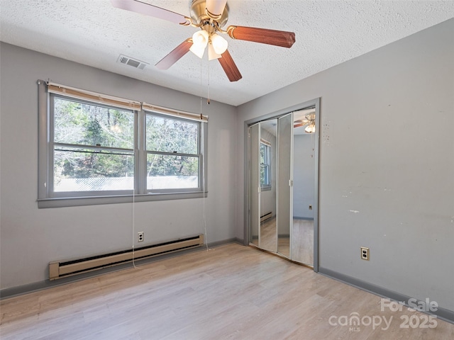 unfurnished bedroom with visible vents, a baseboard radiator, light wood-style floors, a closet, and a textured ceiling