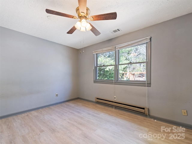 spare room featuring wood finished floors, baseboards, visible vents, a textured ceiling, and baseboard heating