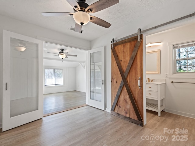 unfurnished bedroom with visible vents, light wood-style flooring, a textured ceiling, a barn door, and baseboards