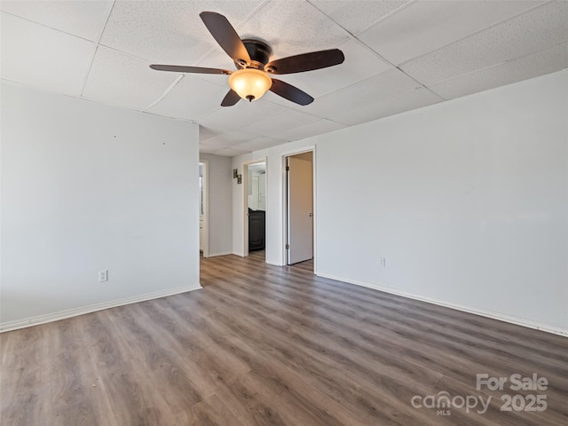 empty room featuring a drop ceiling, baseboards, ceiling fan, and wood finished floors