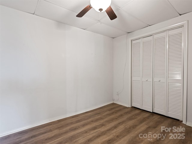 unfurnished bedroom featuring dark wood-type flooring, baseboards, a closet, and ceiling fan