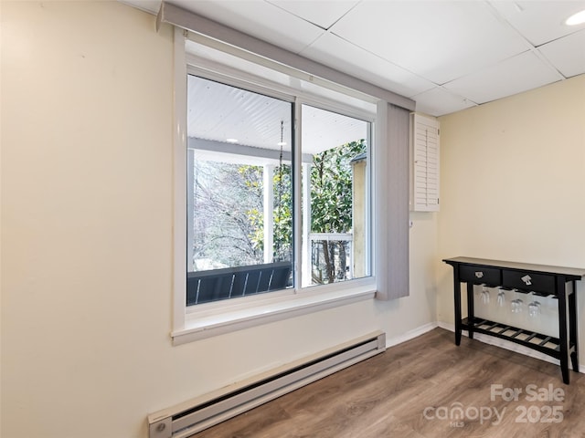 empty room with a paneled ceiling, wood finished floors, baseboards, and a baseboard radiator