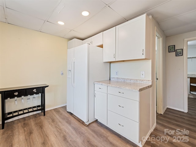 kitchen featuring a drop ceiling, wood finished floors, white cabinetry, white fridge with ice dispenser, and baseboards