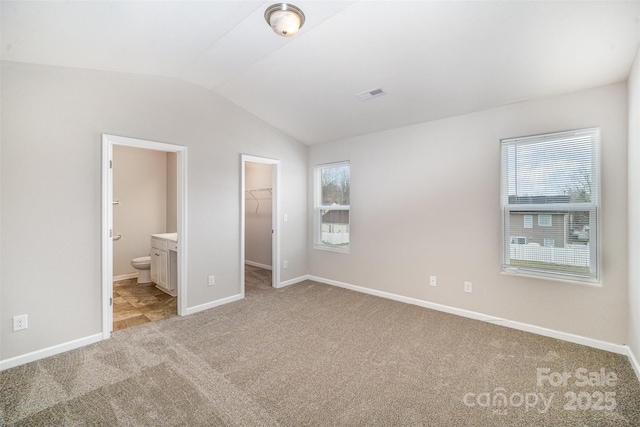 unfurnished bedroom featuring multiple windows, light carpet, a spacious closet, and vaulted ceiling