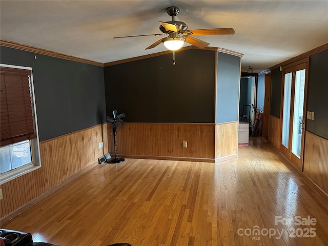 unfurnished room featuring ceiling fan, a wainscoted wall, a healthy amount of sunlight, and wood finished floors