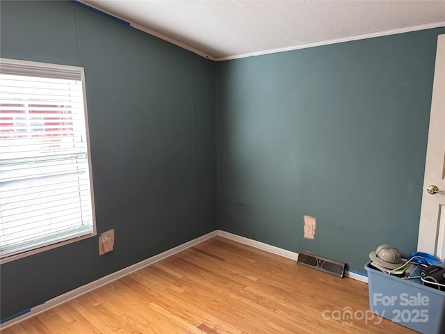 unfurnished room with light wood-type flooring, baseboards, visible vents, and crown molding