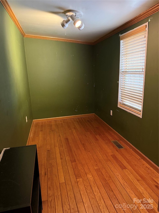 unfurnished room with visible vents, baseboards, crown molding, and hardwood / wood-style flooring