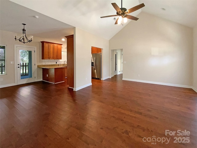 unfurnished living room featuring high vaulted ceiling, ceiling fan with notable chandelier, a sink, dark wood-style floors, and baseboards