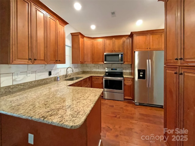 kitchen with brown cabinets, a peninsula, stainless steel appliances, and a sink