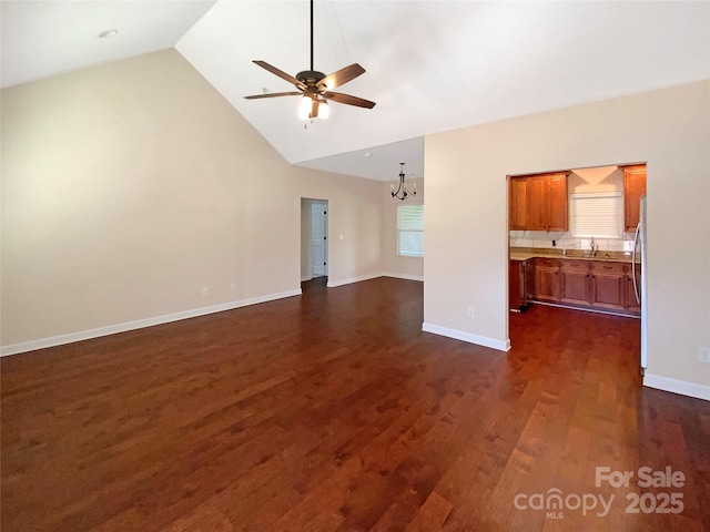 unfurnished living room featuring ceiling fan with notable chandelier, a sink, baseboards, dark wood-style flooring, and vaulted ceiling