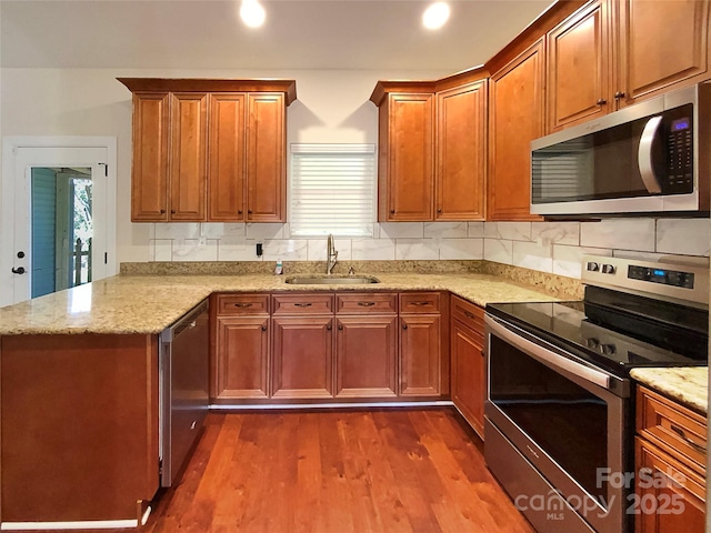 kitchen with backsplash, dark wood-type flooring, a peninsula, stainless steel appliances, and a sink