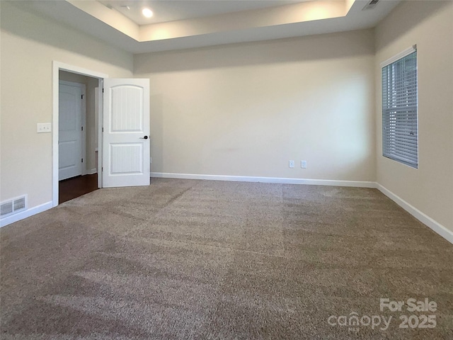 empty room with a tray ceiling, carpet flooring, baseboards, and visible vents