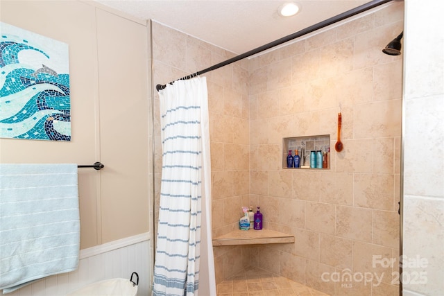 full bath featuring a tile shower and a wainscoted wall