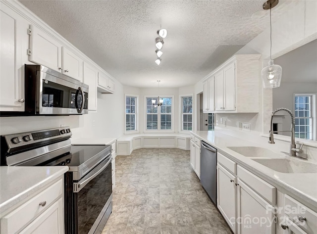 kitchen with appliances with stainless steel finishes, white cabinetry, light countertops, and a sink