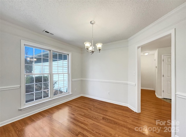 unfurnished room featuring a textured ceiling, crown molding, an inviting chandelier, and wood finished floors