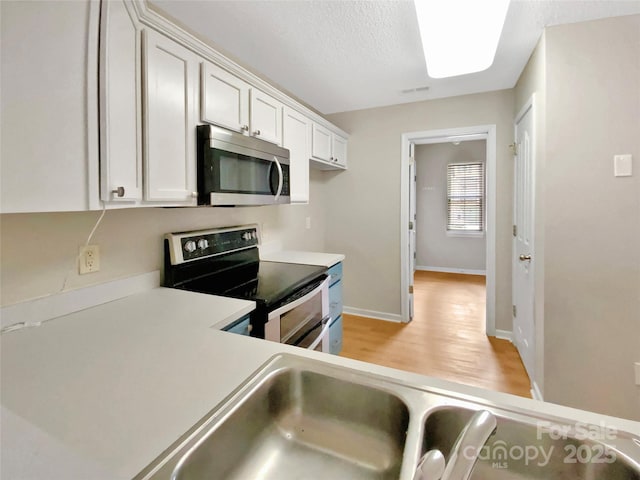 kitchen featuring stainless steel appliances, white cabinetry, light wood-style floors, and light countertops