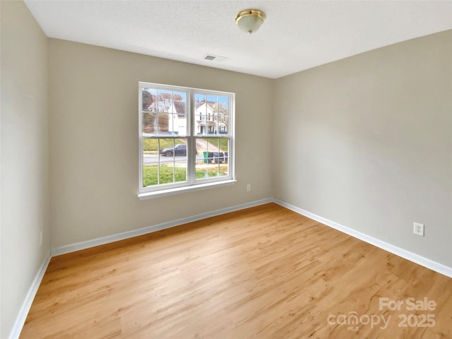 empty room featuring visible vents, wood finished floors, baseboards, and a textured ceiling