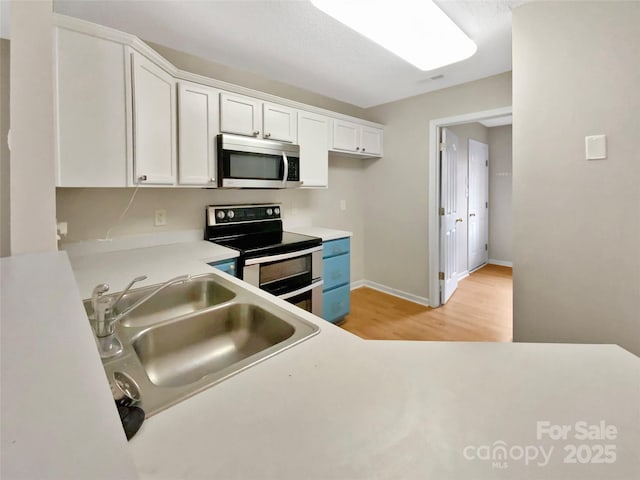 kitchen with light wood finished floors, light countertops, white cabinets, stainless steel appliances, and a sink