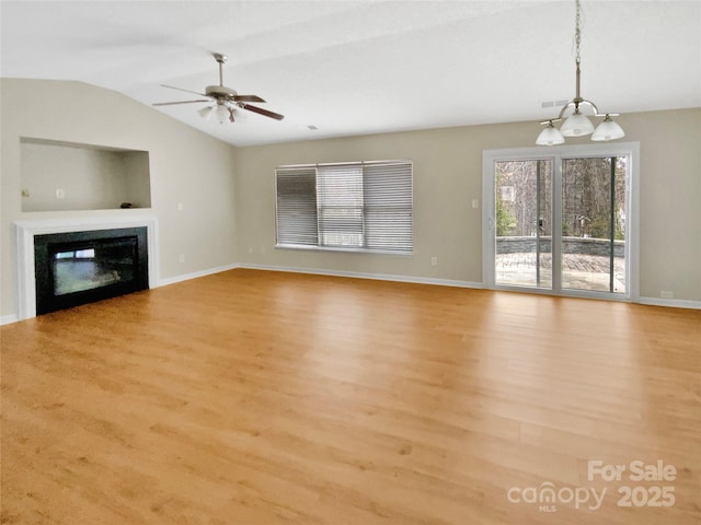 unfurnished living room with wood finished floors, baseboards, vaulted ceiling, a glass covered fireplace, and ceiling fan with notable chandelier