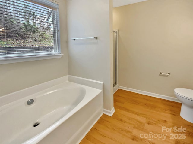 full bath with wood finished floors, baseboards, a stall shower, a garden tub, and toilet