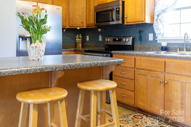 kitchen featuring tasteful backsplash, a breakfast bar area, a sink, appliances with stainless steel finishes, and brown cabinets
