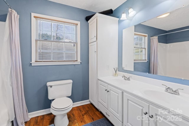 bathroom with baseboards, toilet, wood finished floors, and a sink