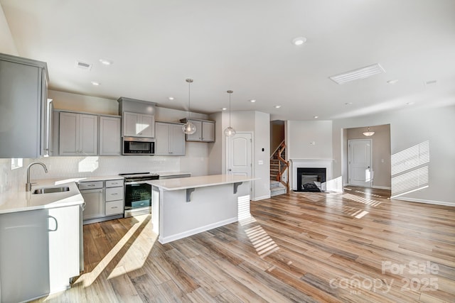 kitchen with gray cabinets, a sink, stainless steel appliances, tasteful backsplash, and light wood-type flooring