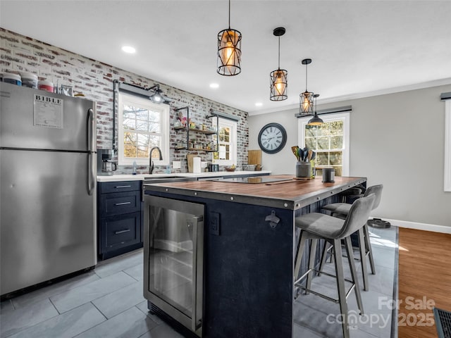 kitchen featuring freestanding refrigerator, wine cooler, a breakfast bar area, butcher block counters, and a healthy amount of sunlight