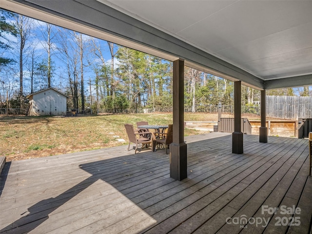 wooden terrace with an outbuilding, outdoor dining area, a fenced backyard, and a lawn