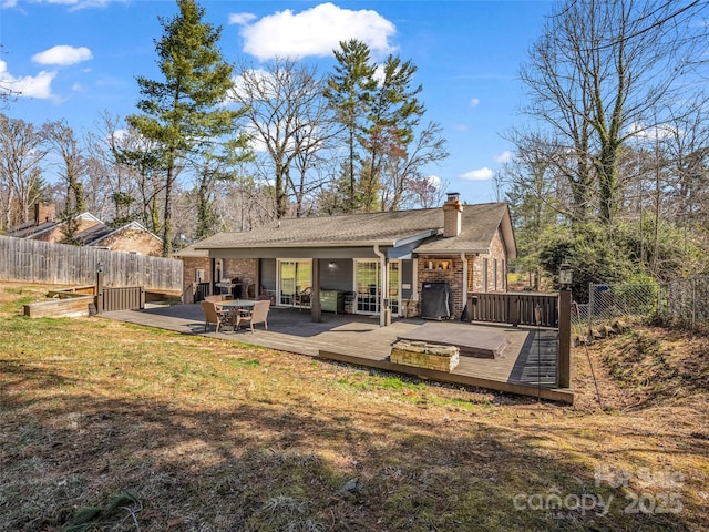 rear view of property with a yard, fence, a chimney, and a wooden deck