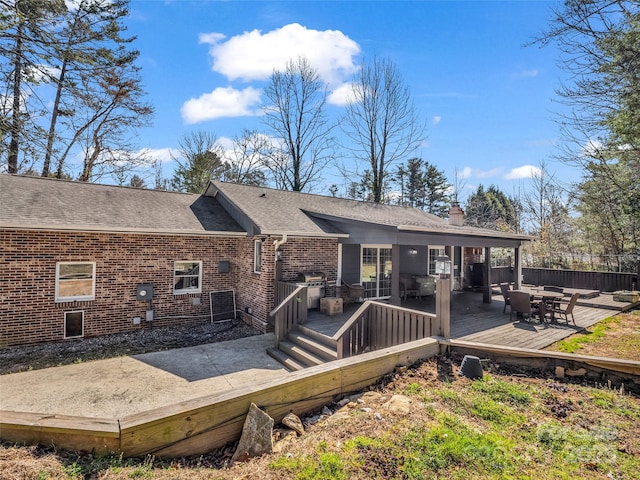 rear view of house featuring brick siding, a deck, a chimney, and a shingled roof