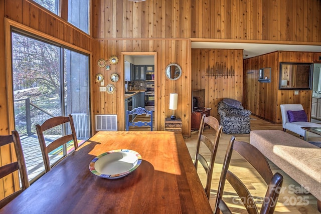 dining space with visible vents, a high ceiling, and wooden walls