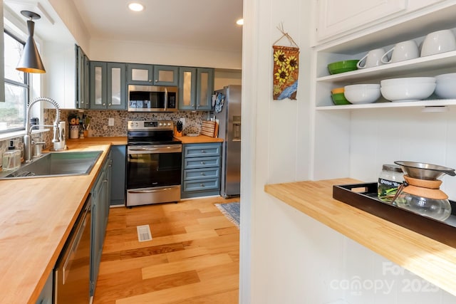 kitchen with a sink, appliances with stainless steel finishes, wood counters, light wood-type flooring, and backsplash