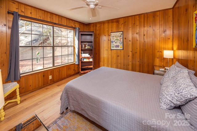 bedroom featuring a textured ceiling, wood finished floors, a ceiling fan, and wood walls