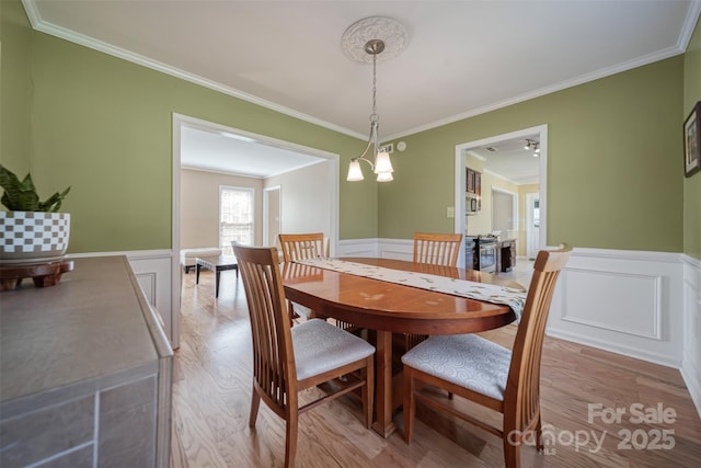 dining room featuring ornamental molding, a wainscoted wall, and light wood-type flooring