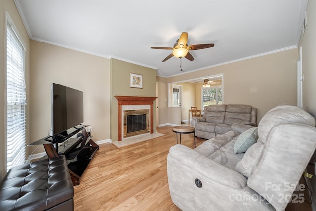 living area with crown molding, baseboards, a fireplace, light wood-style floors, and a ceiling fan