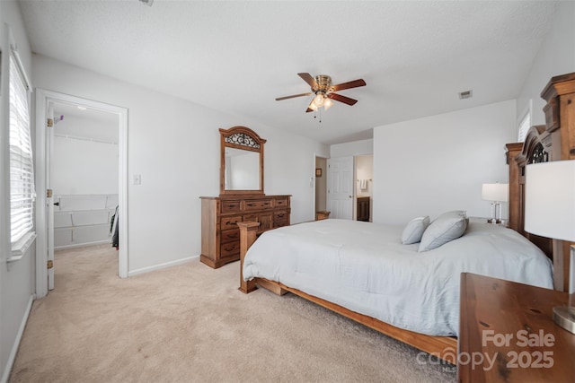 bedroom with visible vents, a walk in closet, baseboards, light colored carpet, and ceiling fan