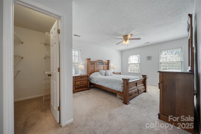 bedroom with visible vents, light colored carpet, a textured ceiling, and a ceiling fan