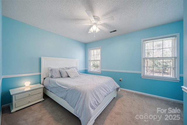 carpeted bedroom with visible vents, baseboards, a textured ceiling, and a ceiling fan