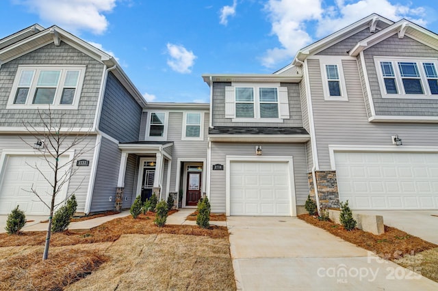 townhome / multi-family property with an attached garage, stone siding, and driveway