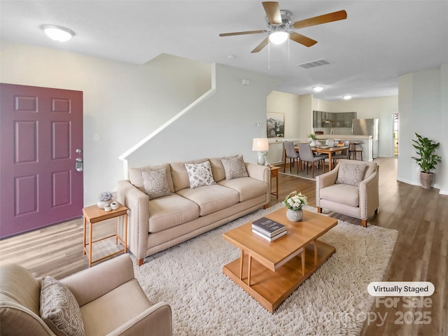 living room with visible vents, wood finished floors, baseboards, and ceiling fan