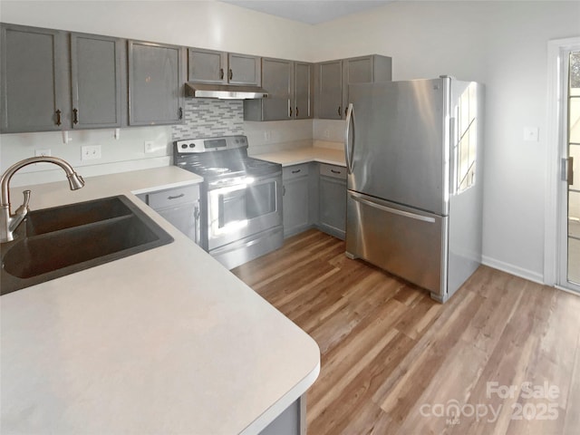 kitchen with a sink, stainless steel appliances, light wood-type flooring, and under cabinet range hood