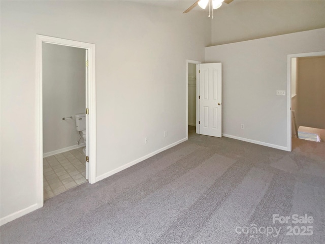 unfurnished bedroom featuring baseboards, carpet, ensuite bathroom, a towering ceiling, and a ceiling fan